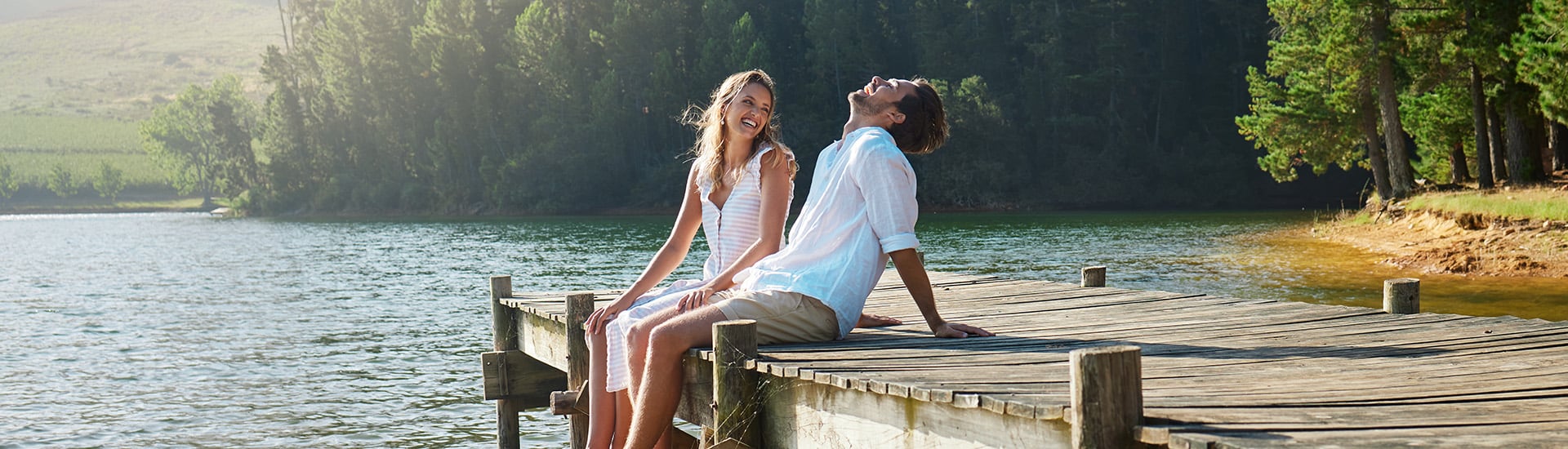 Двойка седи на слънце на кей в езерото и се наслаждава на почивката - с туристическа застраховка.