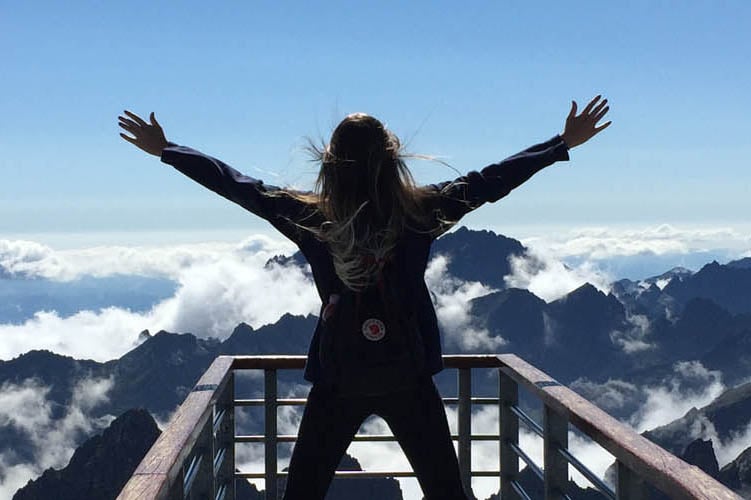 Медицинска застраховка със защита при отмяна на пътуване, турист на планина с ръце във въздоха