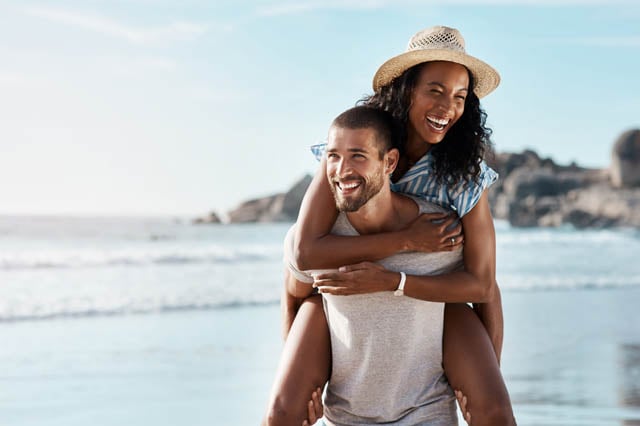 Мъж с бяла тениска и жена с сламена шапка па плаж