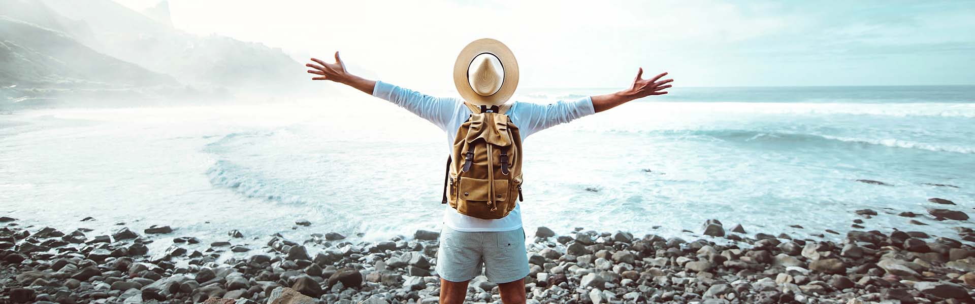 Жена с слънчева шапка на приключенска ваканция, хвърля ръце във въздуха на плажа и се наслаждава на приключенията си.