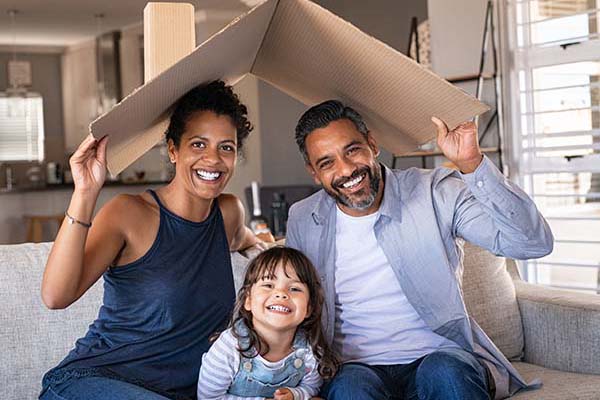 Семейство с дете, добре защитено в своята всекидневна, държи картон във вид на къща над всички глави