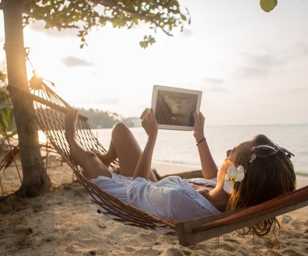 Жена на почивка, лежаща в хамак на плажа, с таблет