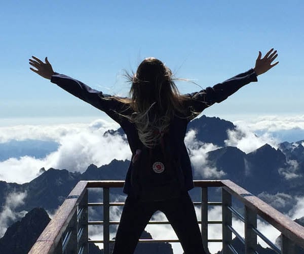 Медицинска застраховка със защита при отмяна на пътуване, турист на планина с ръце във въздоха