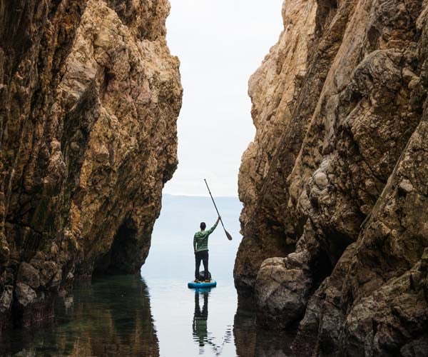 Човек на почивка в чужбина, сърфиращ с гребло в изправено положение