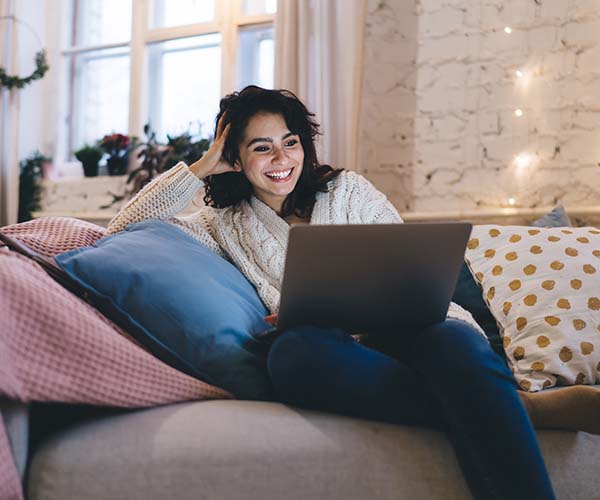 Жена седнала на диван гледа нещо на лаптопа